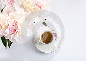 Small bouquet of peonies and old porcelain cup with coffee on a light lilac wooden table. Flat lay