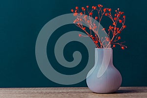 Small bouquet of red flowers in vintage vase on wood table blue navy wall background. Styled stock image mockup for text artwork