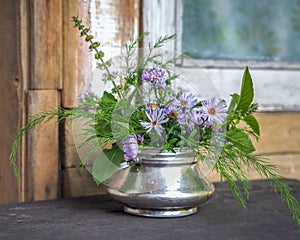 A small bouquet of wildflowers and blue New Belgian asters in a metal sugar bowl