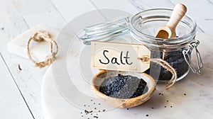 A small bowl of black Hawaiian rock salt on a white marble slab.