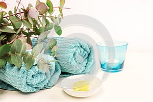 Small bowl with cosmetic moisturizer or emollient for pedicure and soft foot skin, blue towels, candle and some green twigs on a