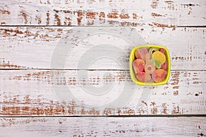 Small bowl with gummy candies on white wooden  background