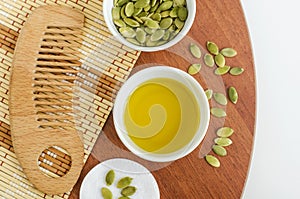 Small bowl with pumpkin seed oil, cotton pad and wooden hair brush. Ingredients for preparing homemade face or hair mask.