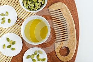 Small bowl with pumpkin seed oil, cotton pads and wooden hair brush. Ingredients for preparing homemade face or hair mask.