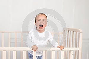A small boy 2 years old is crying in the crib, parents do not approach the crying baby
