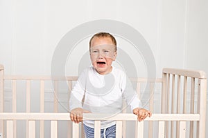 A small boy 2 years old is crying in the crib, parents do not approach the crying baby