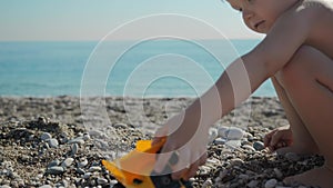 A small boy of 5 years old is playing on the beach near the sea with a toy truck
