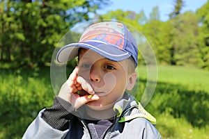 Small boy in baseball cap blowing to the footstalk