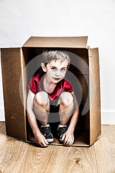 Small boy in cardboard box hiding for sad moving day