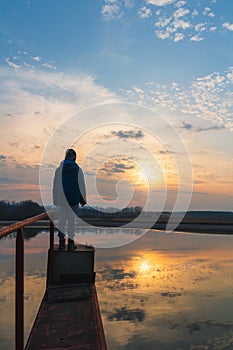 Small boy, child in jacket standing on water gate pond shore at sunset. Czech landscape