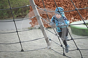 Small boy is climbing the rope ladder at playground in spring