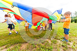 Small boy is covering kids with colorful parachute