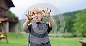 Small boy with dirty hands standing in vegetable garden, sustainable lifestyle.