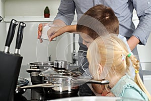 Small boy with girl l salting food with father in the kitchen