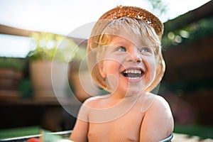 Small boy with a hat outdoors in garden in summer, laughing. Copy space.