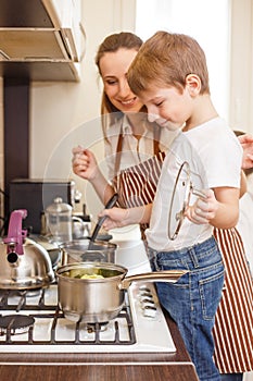 Small boy with his mother cooking in pot on hob