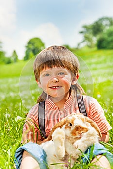 Small boy hugging rabbit in green field