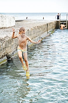 Small boy jumps from stone pier to sea touching water