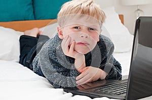 Small boy laying on his bed looking at his laptop