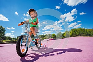 Small boy learn to ride bicycle with learning wheels, low angle