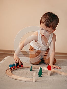 Small boy makes a choo-choo train with mouth while sitting on the floor and playing with a wooden train toy