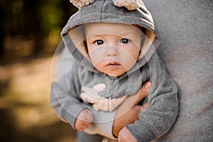 Small boy with pensive gray eyes looks attentively sitting at the fathers hands