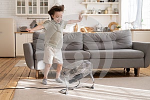 Small boy play with strong wind blow from ventilator or retro fan at home in cozy living room alone