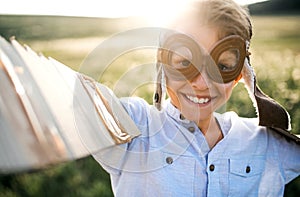 A small boy playing on a meadow in nature, with goggles and wings as if flying.