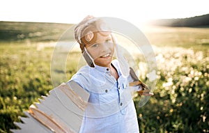 A small boy playing on a meadow in nature, with goggles and wings as if flying.