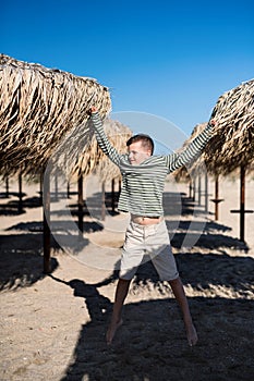 A small boy playing outdoors on sand beach, jumping.