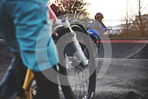 small boy with protective gear has fun with a stunt scooter on an modern asphalted pump track in bright evening light.