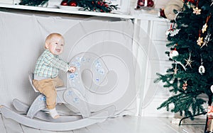 Small boy riding a horse in white room decorating for Christmas and winter holidays. Playing alone and having fun. Part