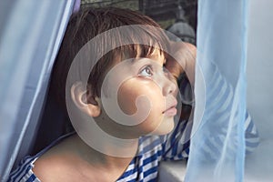 Small boy on self-isolation looks out the window with hope