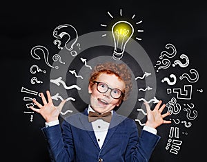 Small boy student with question marks and light bulb on blackboard background