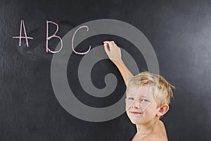 A small boy without a T-shirt writes ABC on the blackboard