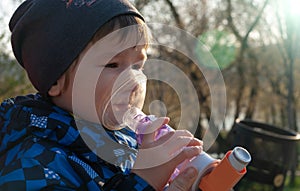 A small boy who suffering from illness bronchial asthma getting treatment with aerosol inhaler outdoors