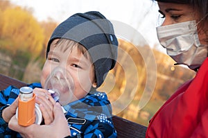 A small boy who suffering from illness bronchial asthma getting treatment with aerosol inhaler outdoors