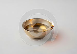Small brass oil lamp with a lit flame on a white background