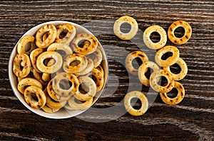 Small bread rings with poppy in bowl and scattered bread rings on wooden table. Top view