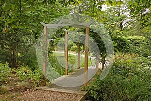 A small bridge with a wooden archway crosses a small stream in a quiet English garden