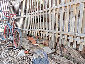 a small broken bicycle leaning against a bamboo fence