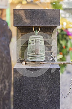 Small bronze bell hanging at the foot of Habataki Kanzeon Bosatsu statue in Tabata Togakuji temple in Tokyo