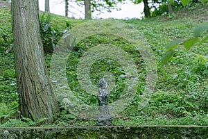 A small bronze Bodhisattva statue in a green forest in Lushan Mountain, China.