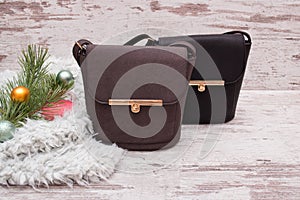 Small brown and black female handbag on a wooden background, fir branch with decorations