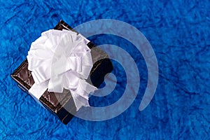 Small brown colored gift box with white ribbon bow and blue background. Wedding gifts concept