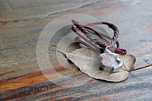 Small buddha amulet in the frame with the rope necklace for the neck on the dry Bodhi leaf on the wooden table.