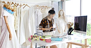 Small Business of Asian women Fashion Designer Working and using smart phone and tablet With Wedding Dresses at at clothing store