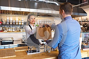 Small business and entrepreneur concept with smiling young waitress wearing black apron serving customer at counter in restaurant