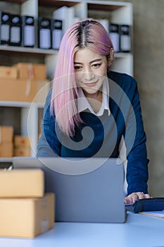 Small Business Entrepreneur SME owner cute young asian woman checking orders with laptop computer using smartphone checking orders