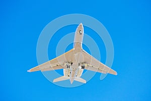 Small business jet with landing lights and deployed landing gear preparing for landing at airport. Blue sky